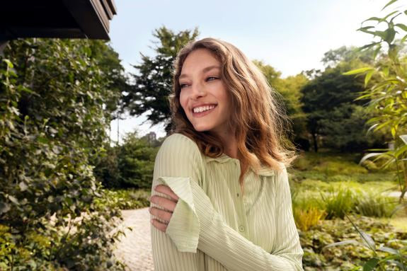 Lächelnde junge Frau mit welligem Haar in grüner Bluse in einem Park