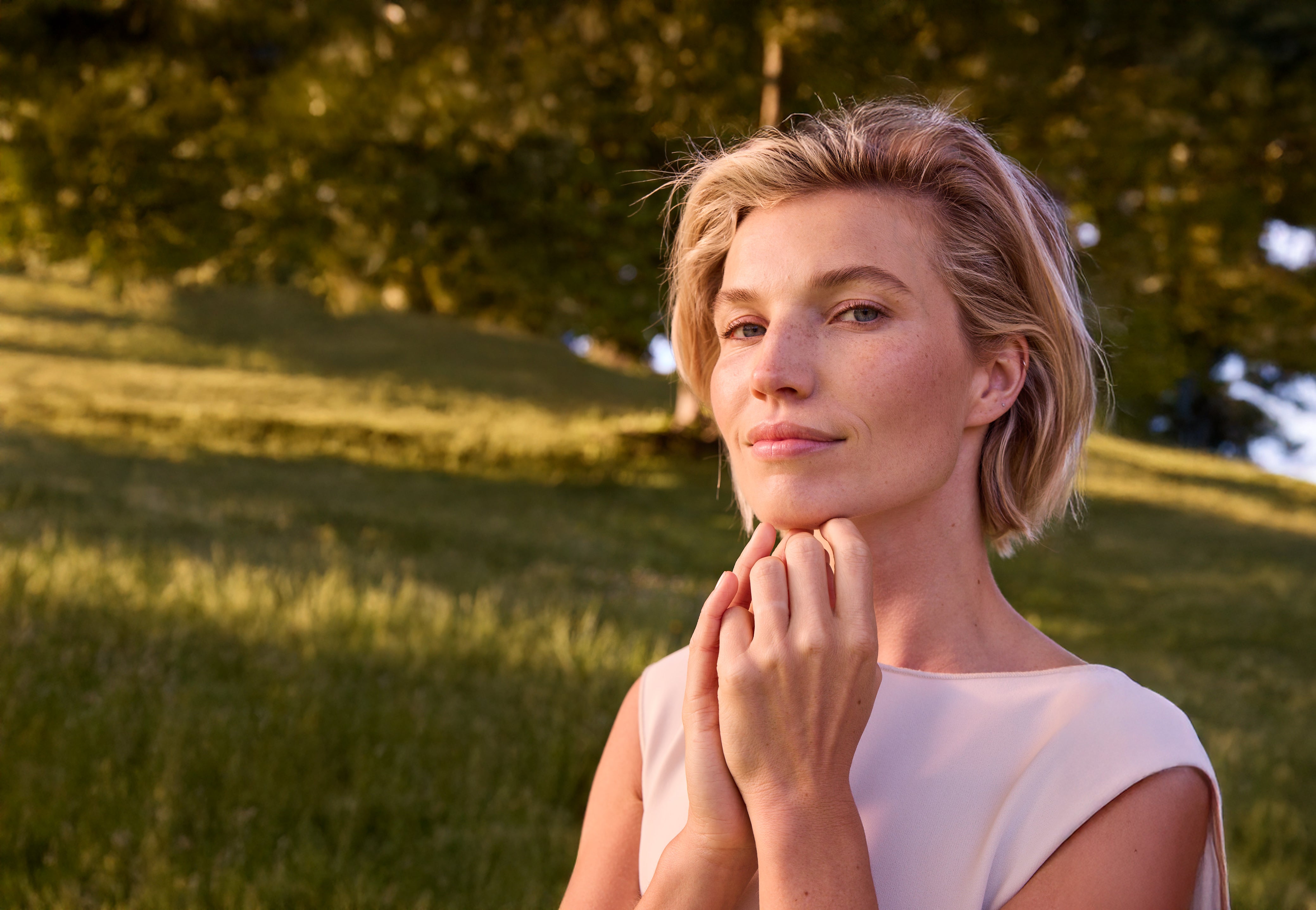 Sinnlich schauendes Model auf einer grünen Wiese und vor einem Baum