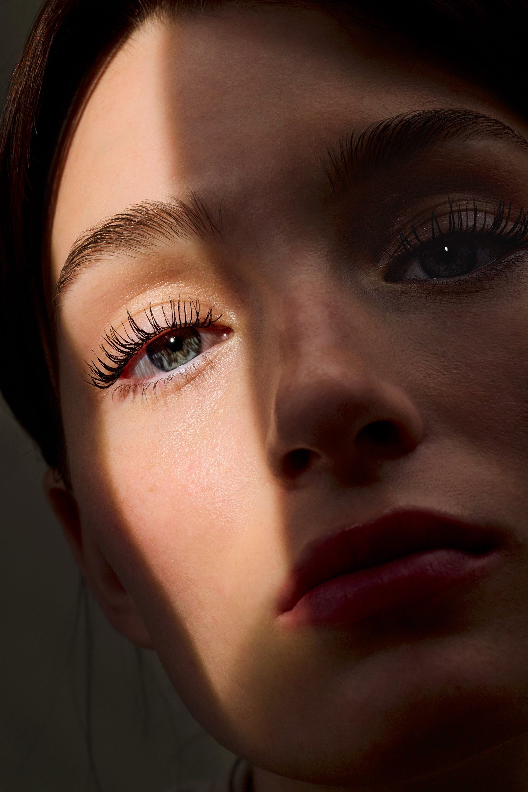 Nahaufnahme eines Gesichts mit Fokus auf die Augenpartie, lange definierte Wimpern, teilweise von Licht und Schatten überlagert.