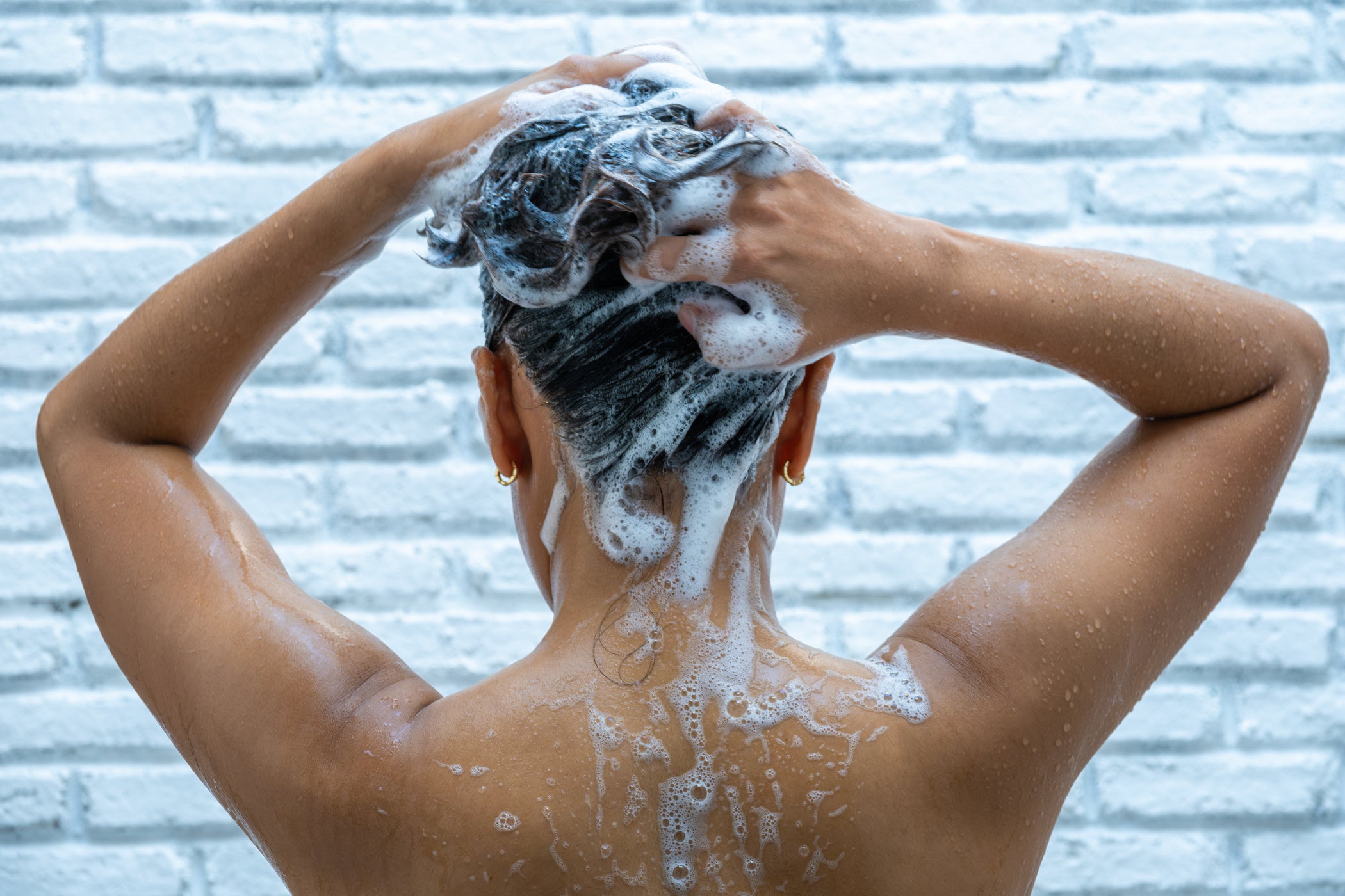 Frau steht in der Dusche und wäscht sich die Haare mit schaumigem Shampoo