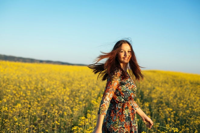 Person geht durch blühendes Rapsfeld im Sonnenlicht.