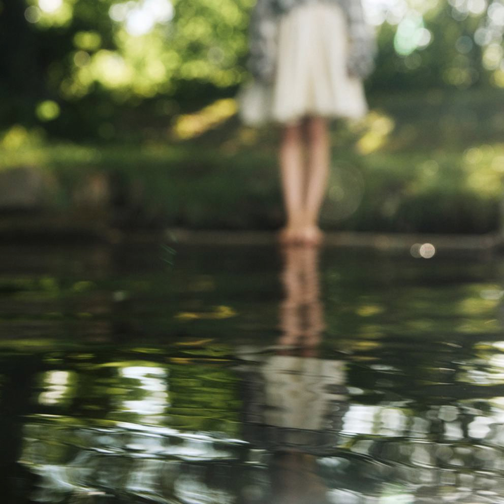 Beine einer Frau in Rock, die sich im Wasser spiegelt