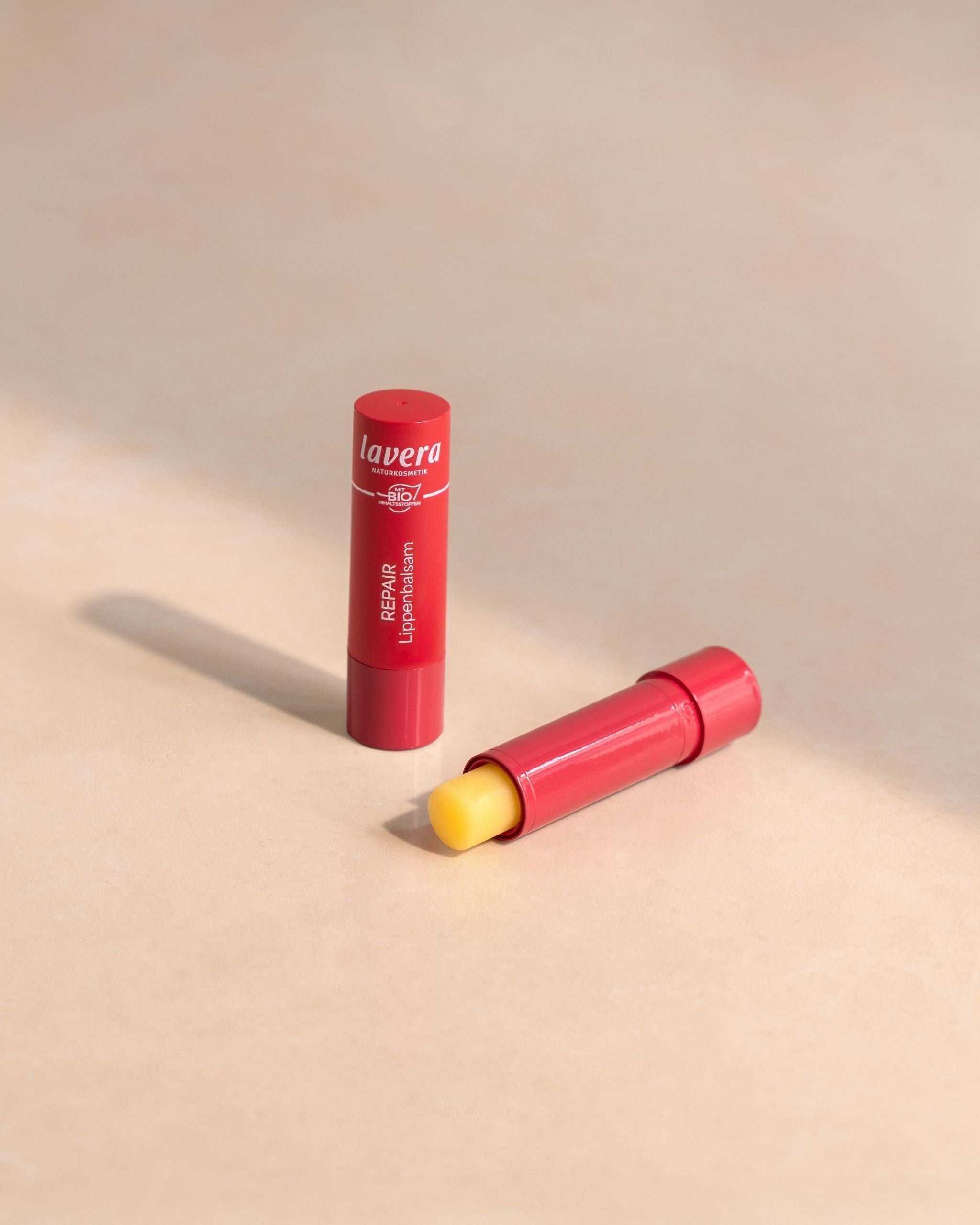 zwei Lavera Repair Lippenbalsame in roter Verpackung, geöffnet und geschlossen auf hellem Untergrund.