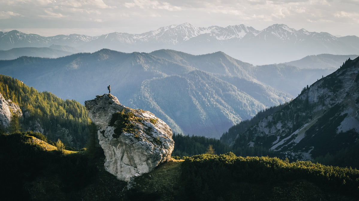 Person steht auf einem großen Felsen in einer grünen Berglandschaft