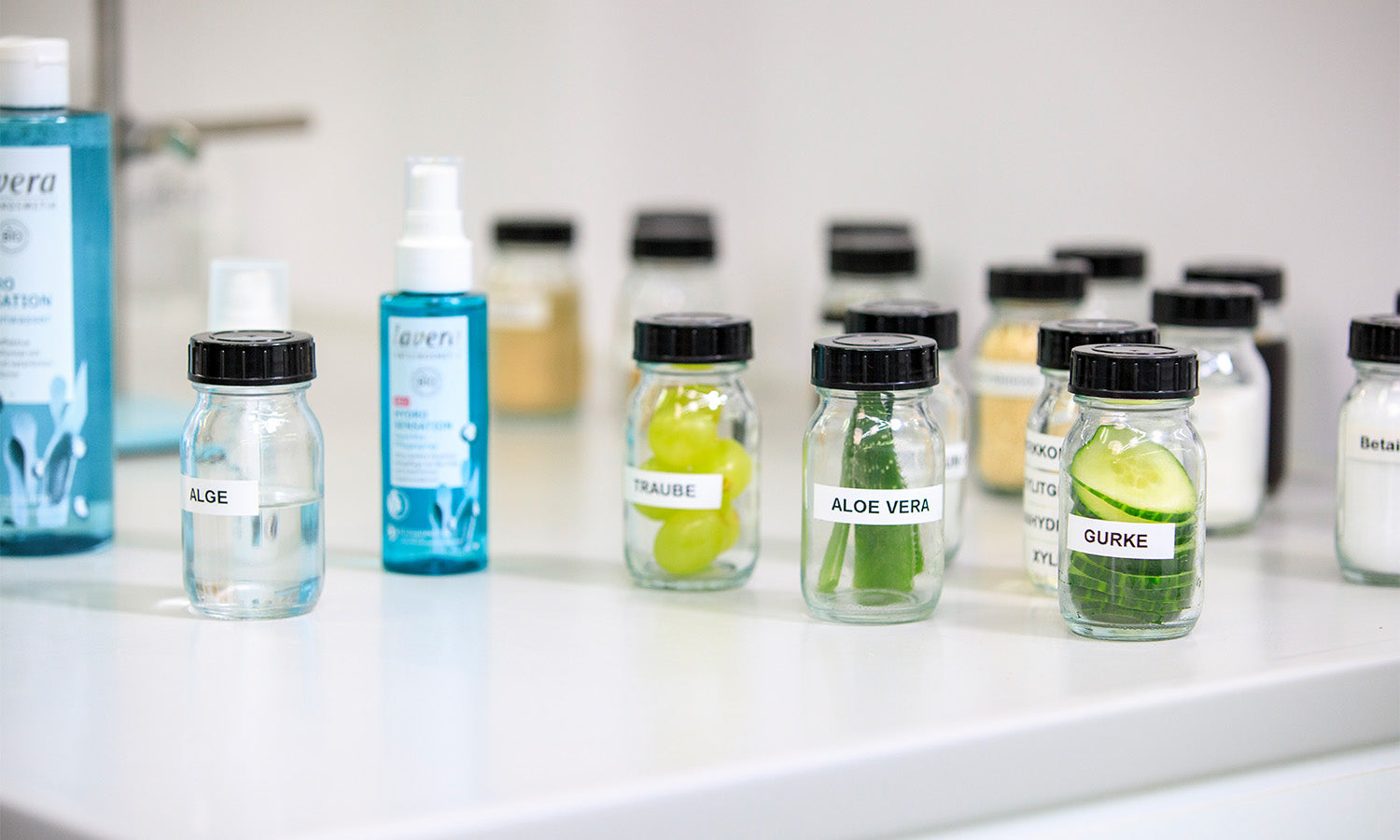 Verschiedene Inhaltsstoffe wie Gurke und Aloe Vera in kleinen Gläsern im Labor