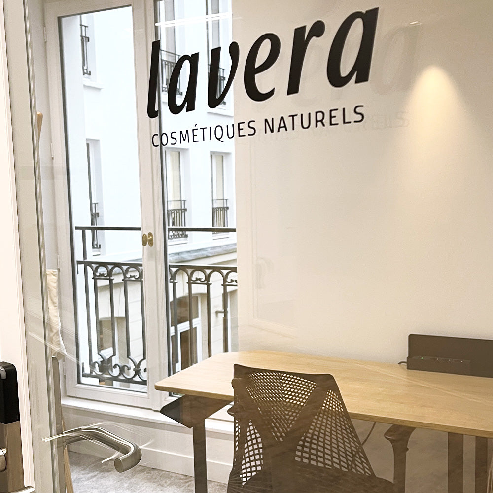 lavera Büro: Schriftzug „Cosmétiques Naturels“ auf Glaswand, Schreibtisch am Fenster