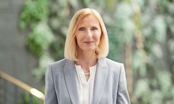 Porträt einer Frau mit freundlichem Ausdruck vor hellem Hintergrund.