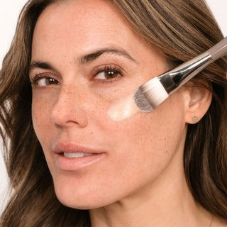 Frau trägt Foundation mit einem Pinsel auf die Wange auf