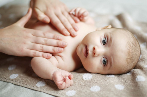Baby liegt auf Decke, Hände massieren sanft den Oberkörper, Babypflege