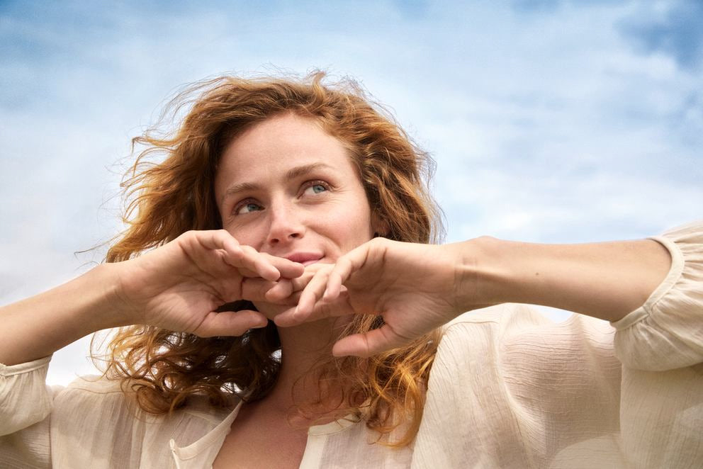 Frau mit lockigem rotem Haar blickt lächelnd in den Himmel