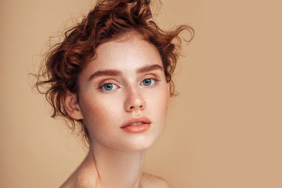 Porträt einer rothaarigen Frau mit Sommersprossen vor beigem Grund