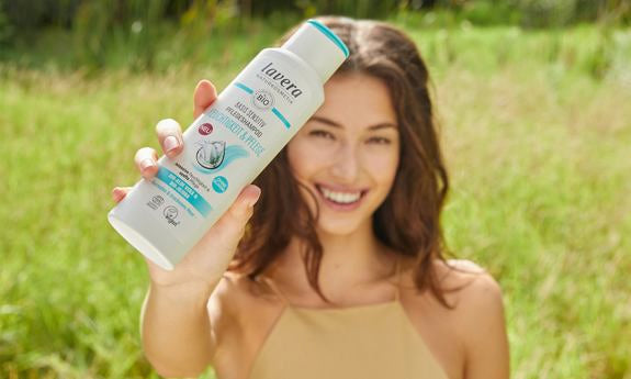 Frau hält lächelnd eine lavera Basis Sensitiv Shampoo-Flasche