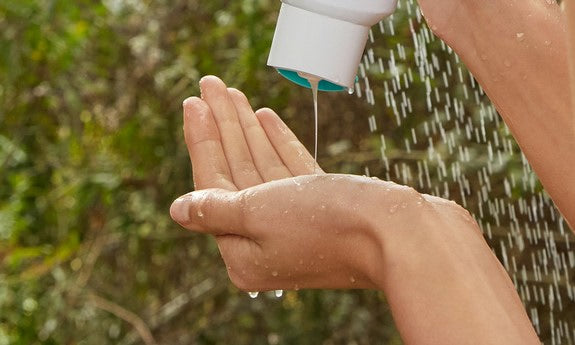 Hand gibt Shampoo aus der Flasche unter fließendem Wasser