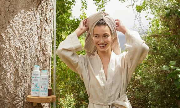 Frau im Bademantel mit Handtuch und lavera Haarpflegeprodukten