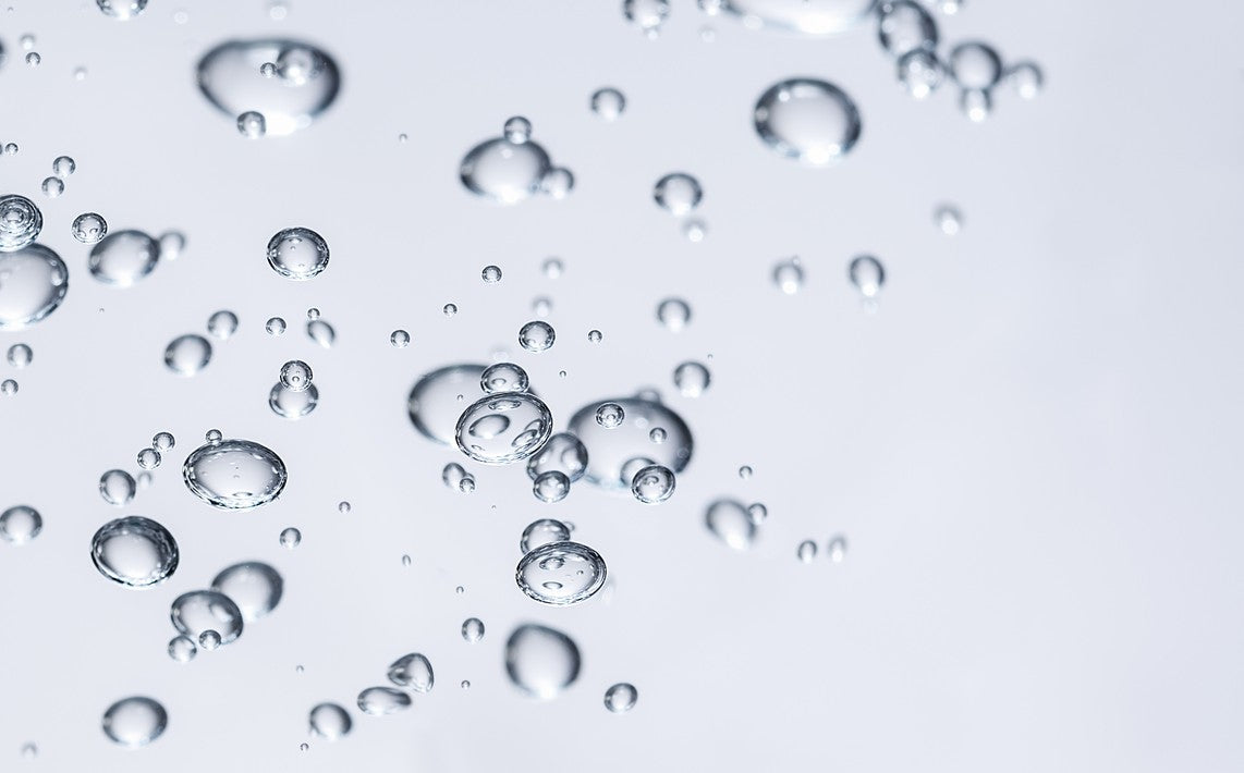 Nahaufnahme von transparenten Glycerinblasen in Flüssigkeit vor hellem Hintergrund.