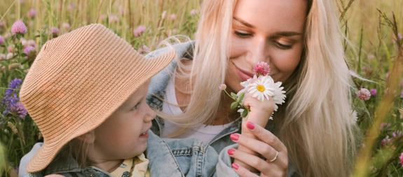 Mutter und Kind riechen an einer Blume auf einer Wiese